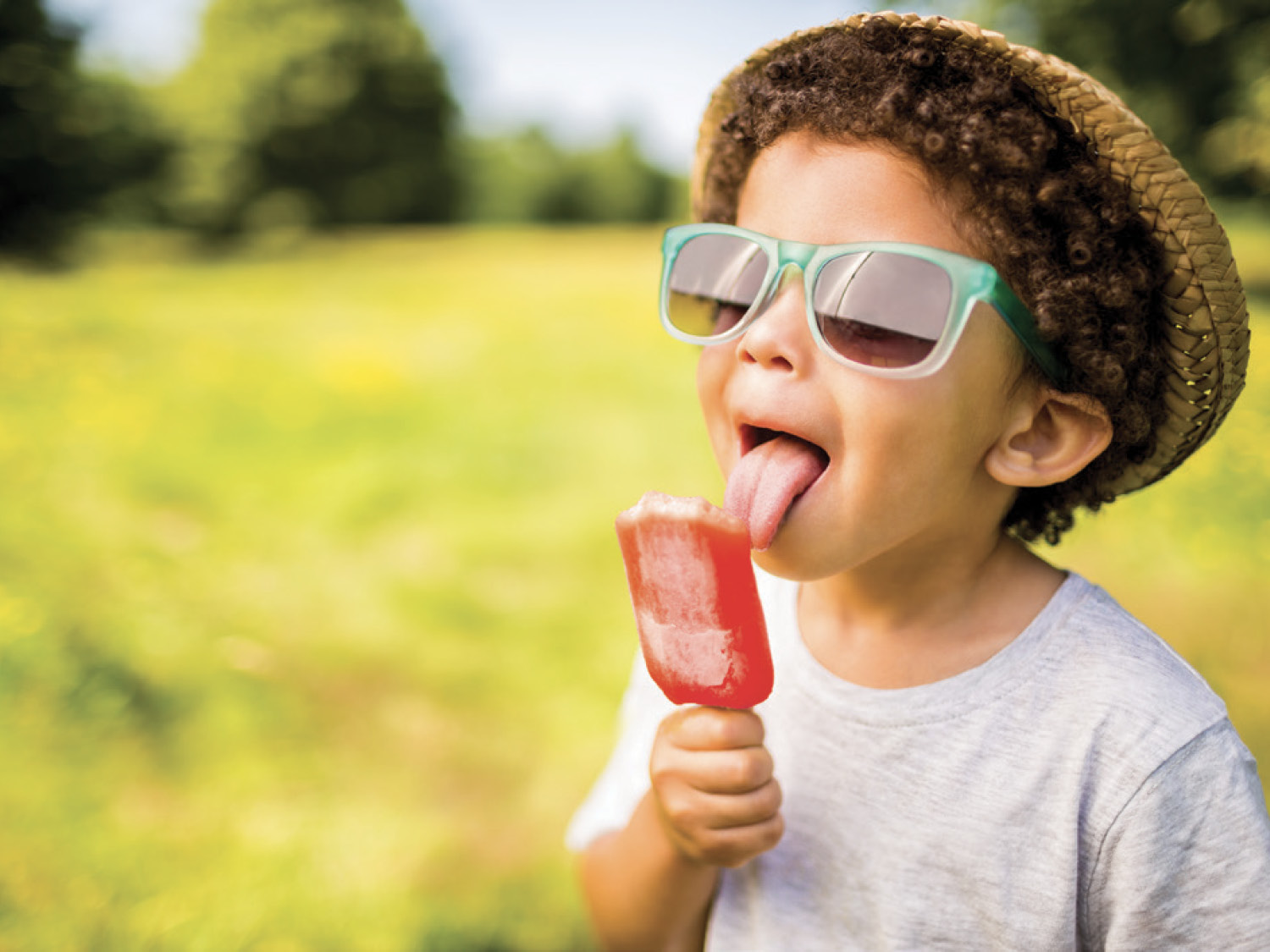 A boy wearing sunglasses holding a red popsicle A boy wearing sunglasses holding a red popsicle