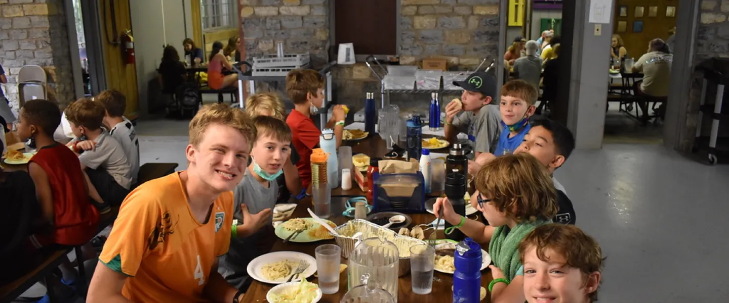 Kids and teens gathered around a table eating a meal at Camp Piomingo