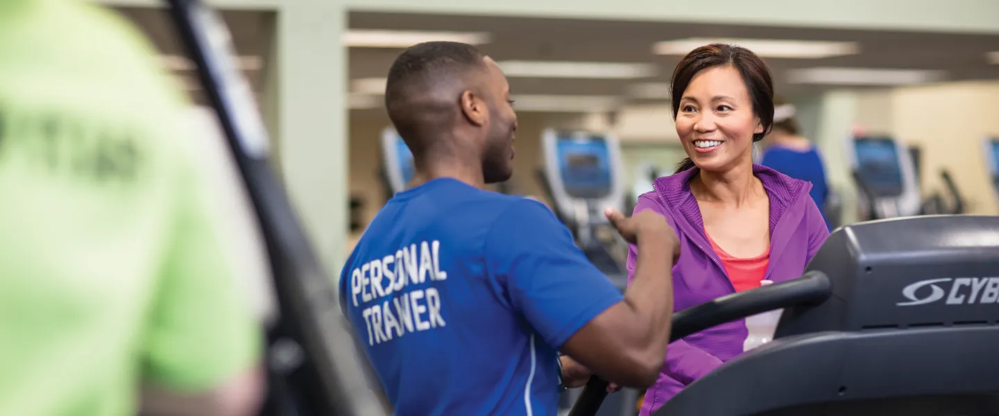 Woman walks on treadmill while personal trainer supervises