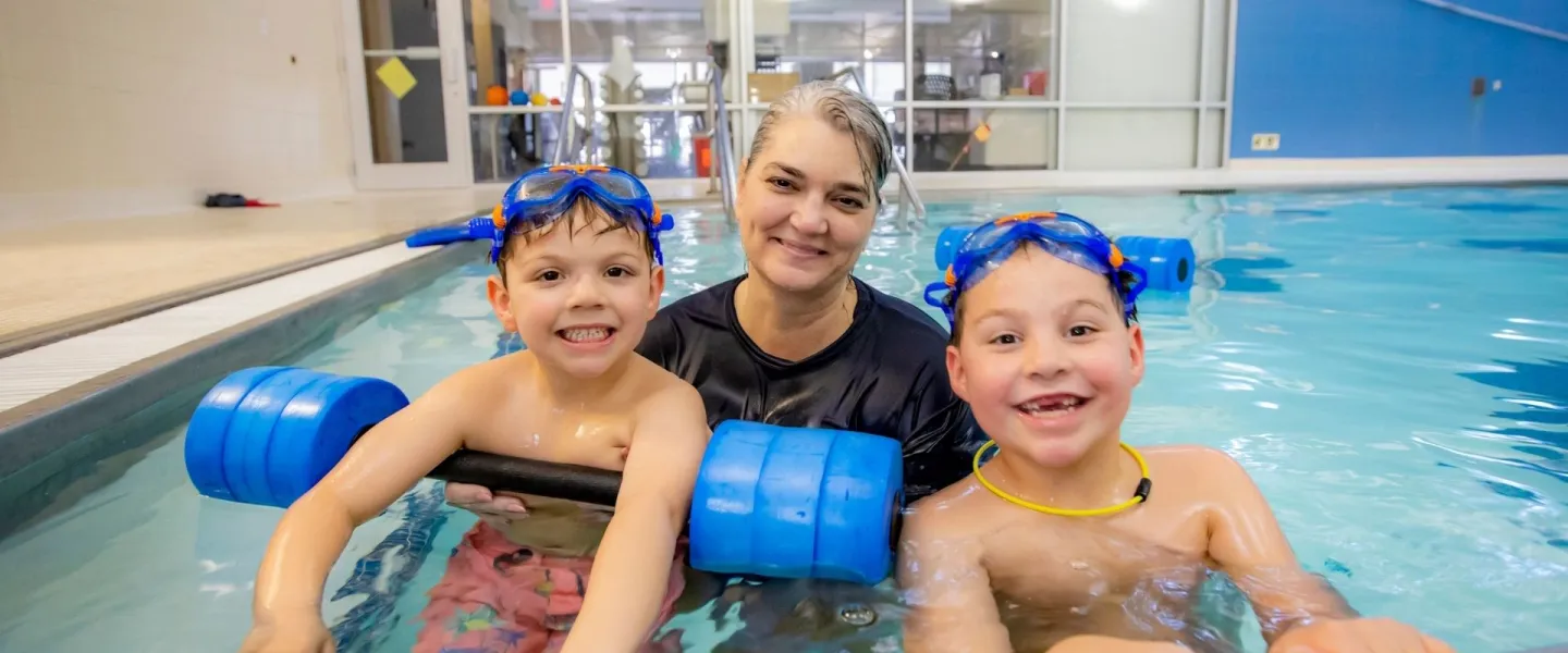 Swim instructor in pool with two smiling young boys