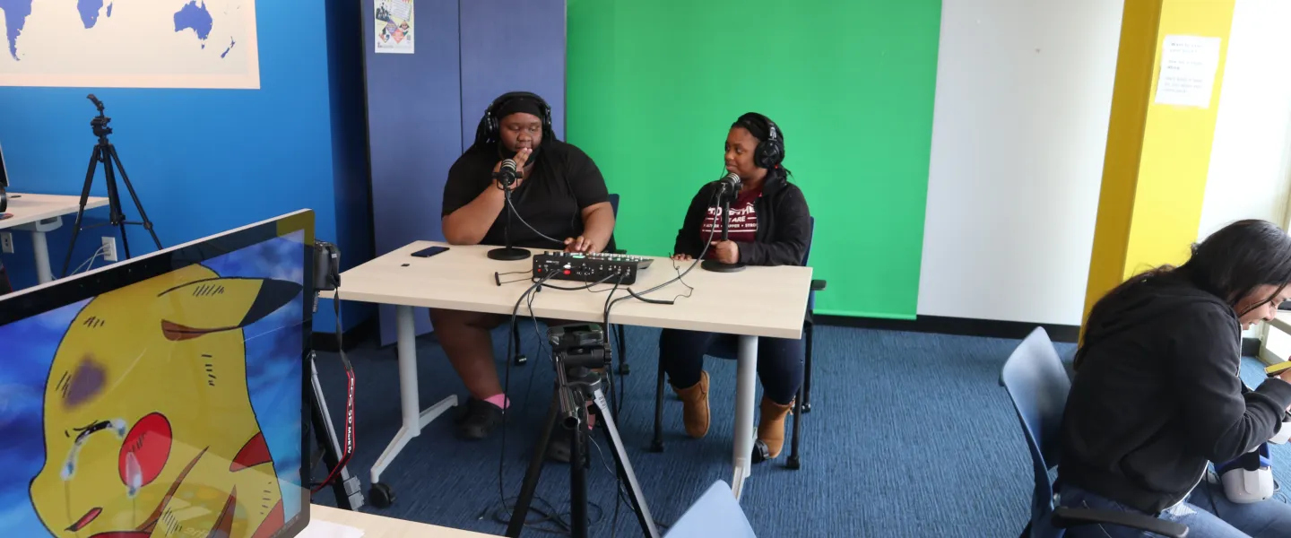 2 teens sitting at a desk recording a podcast