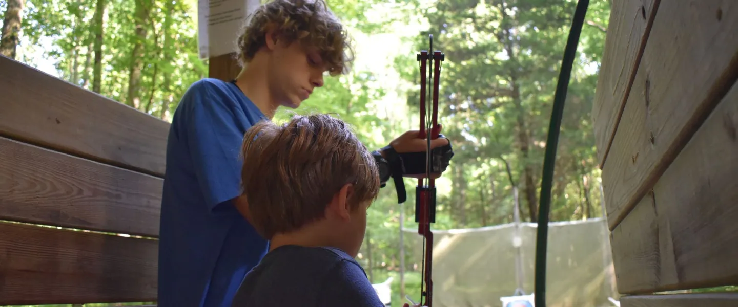 Camp counselor teaching a young camper how to do archery