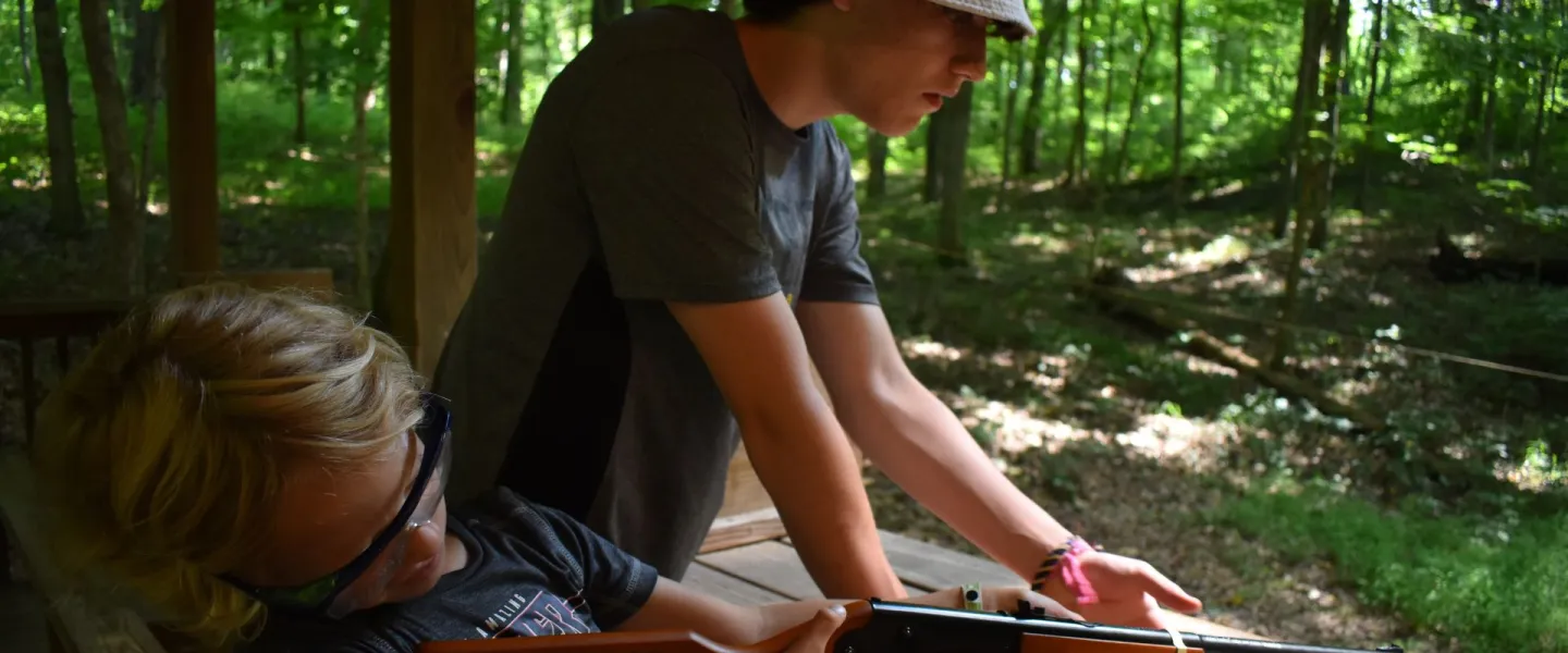 Camp counselor helping camper safely use BB gun at YMCA Camp Piomingo