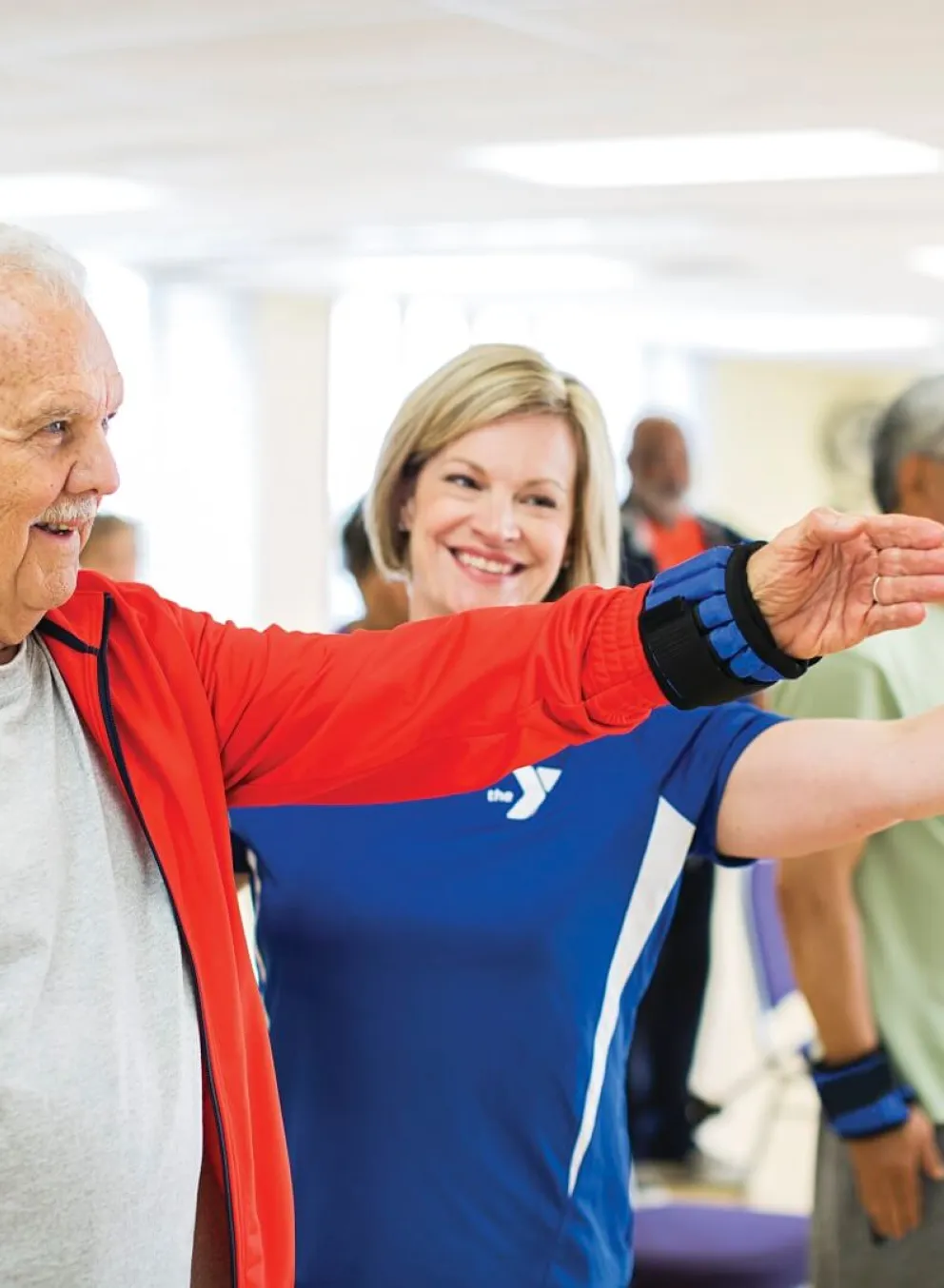 Older man and instructor lifting weighted arm band at YMCA Louisville