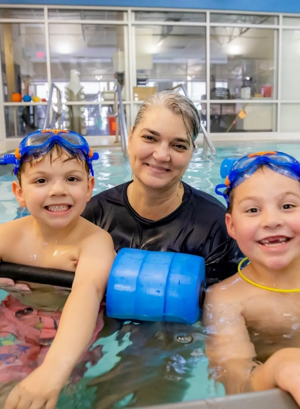 Swim instructor in pool with two smiling young boys