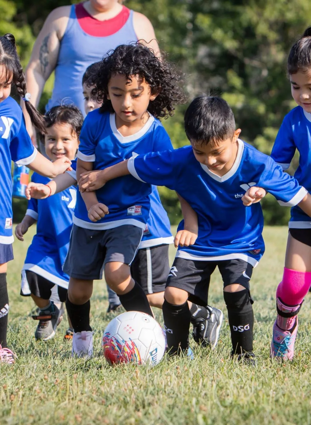 Group of children wearing YMCA soccer uniforms running after soccer ball