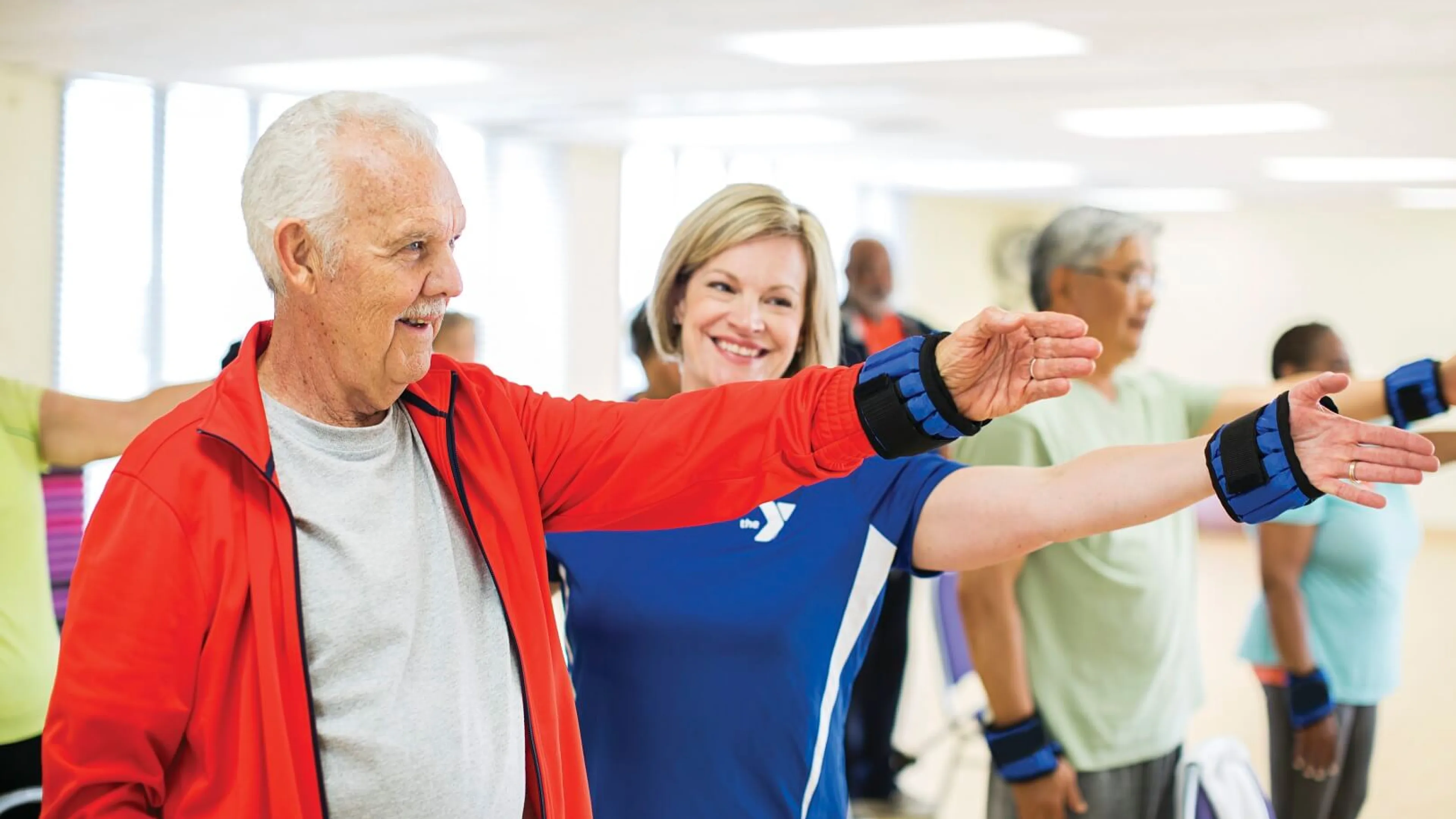 Older man and instructor lifting weighted arm band at YMCA Louisville
