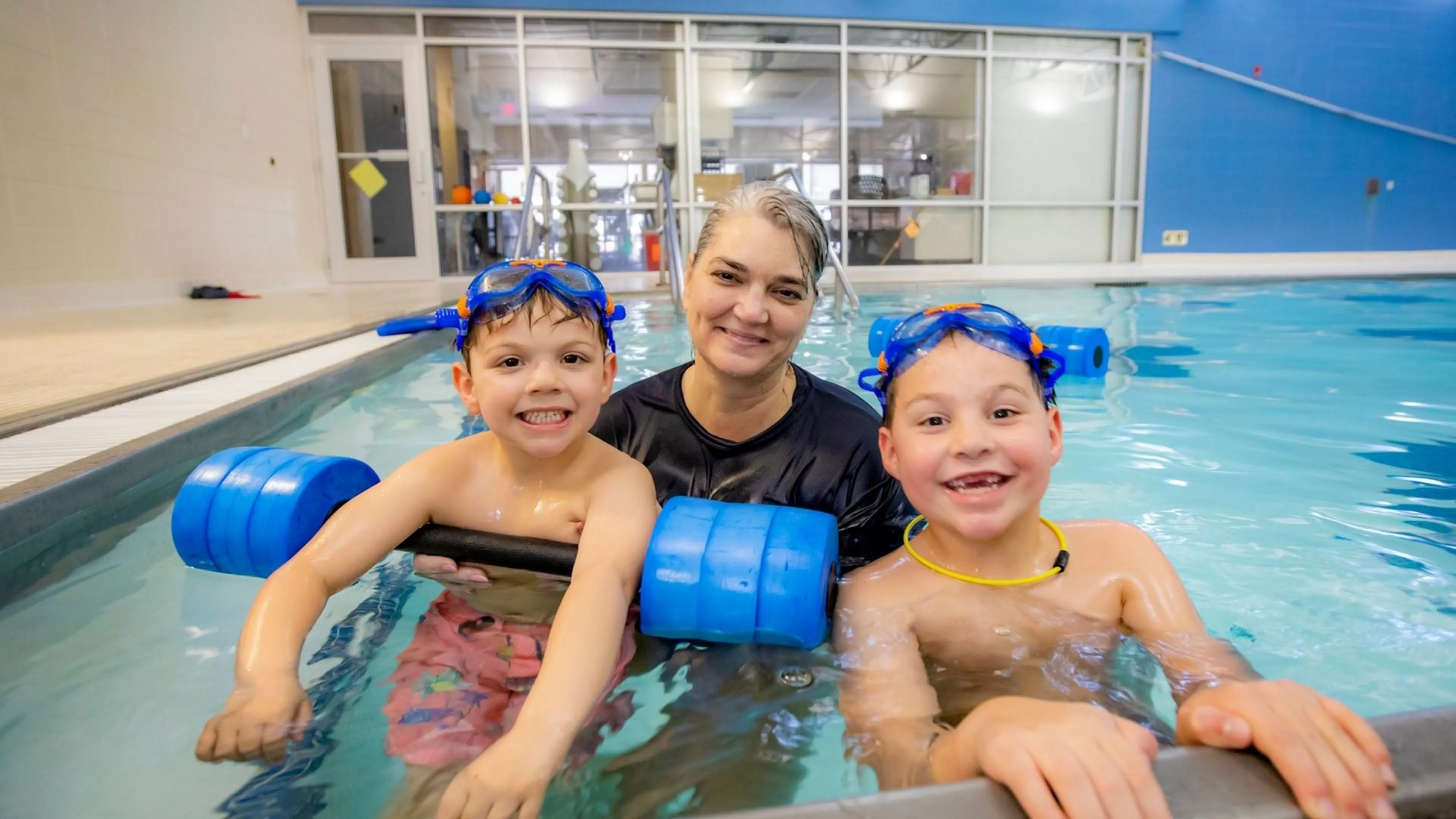 Swim instructor in pool with two smiling young boys