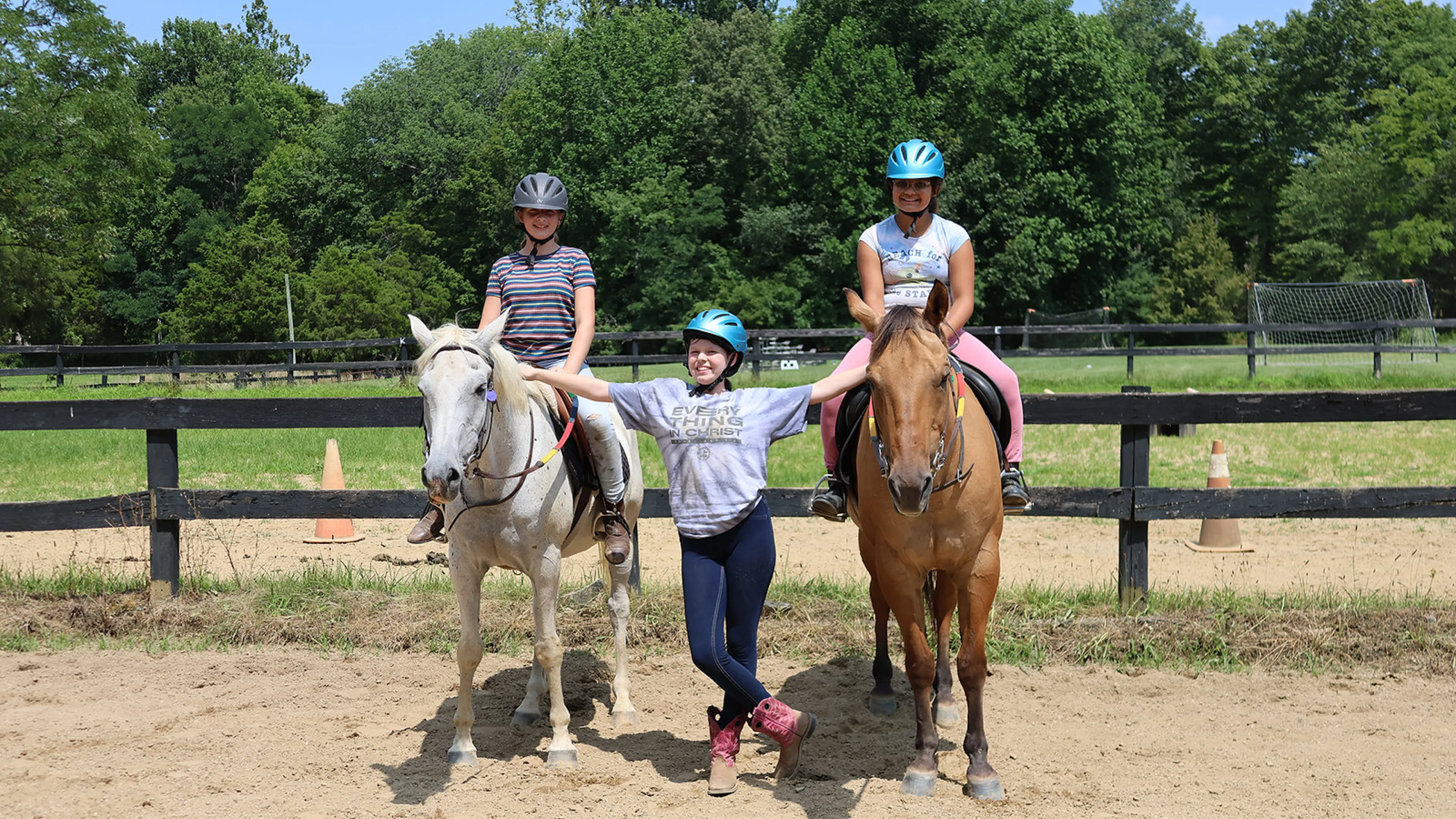 Two girls on horses while another girl is standing next to them