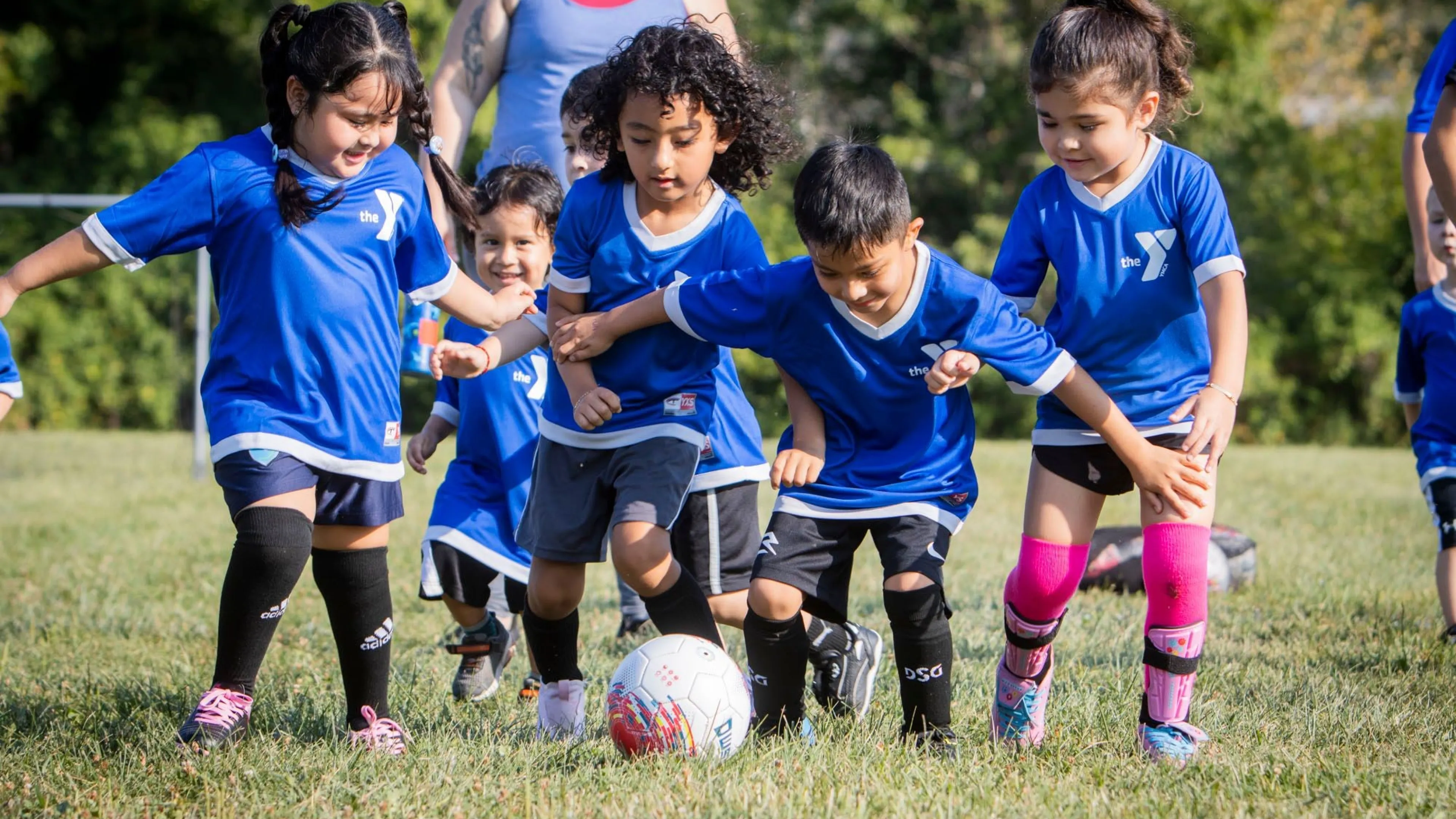 Group of children wearing YMCA soccer uniforms running after soccer ball