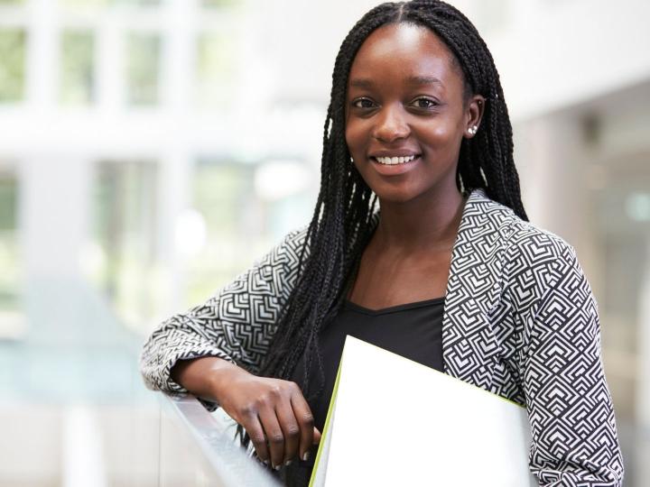 Smiling African American teen learning against railing holding a notebook