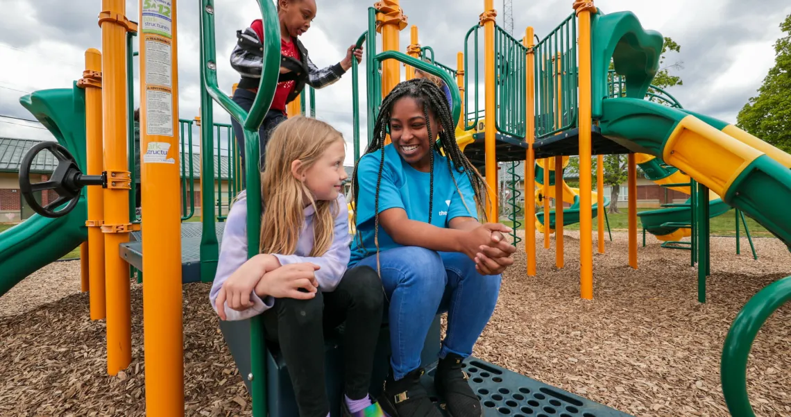 Young woman sitting at a playground talking to a girl